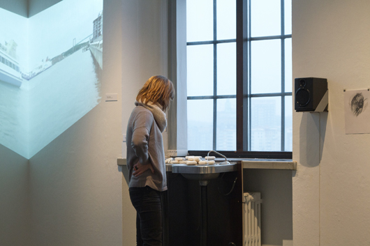 VASKA av Emelie Röndahl ljudsätts av den droppande kranen. På väggen en detalj av videon RITE DE PASSAGE av Jasmine Lyman i samarbete med luftakrobaten Milla Floryd. Foto: Sjöfartsmuseet/Akvariet